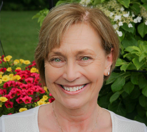 photograph of dental hygienist Mary Nienhouse smiling in front of colorful flowers and a green bush