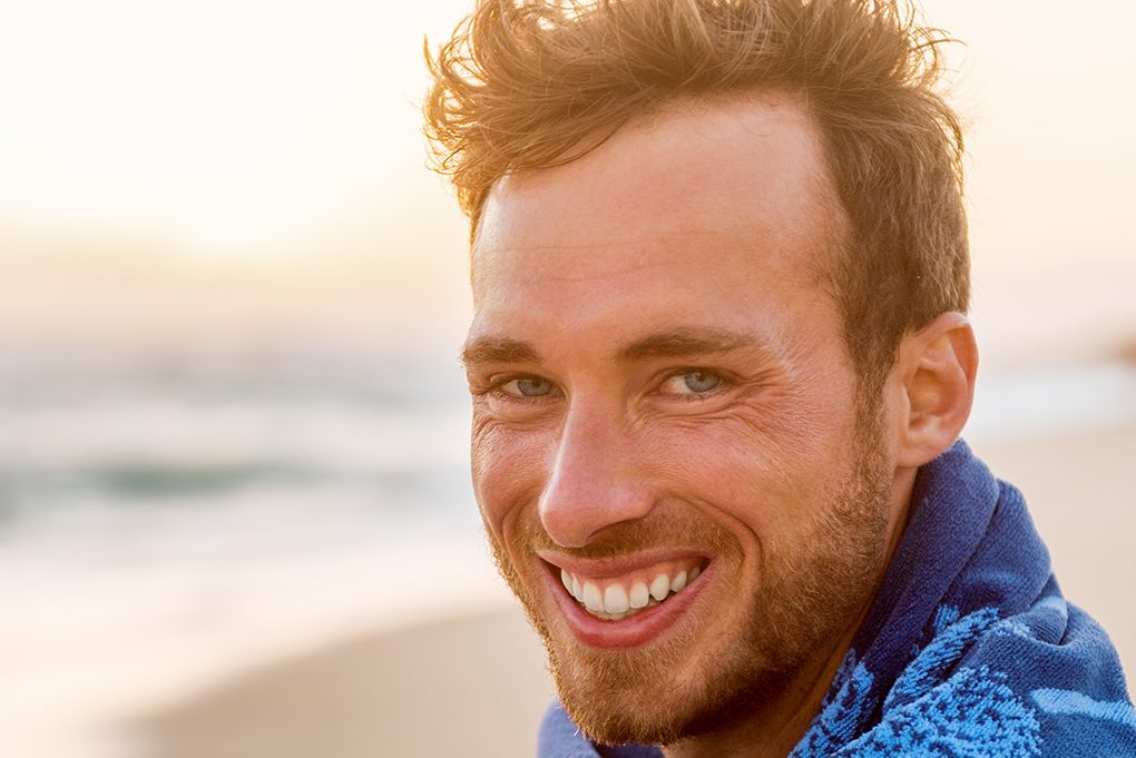 man on the beach smiling widely with the sun shining in the background